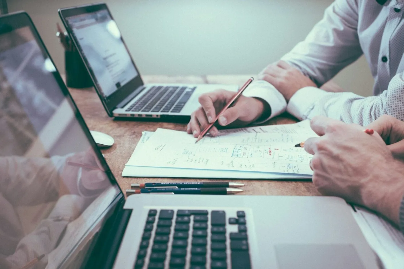 Two people reviewing a project plan on paper beside laptops